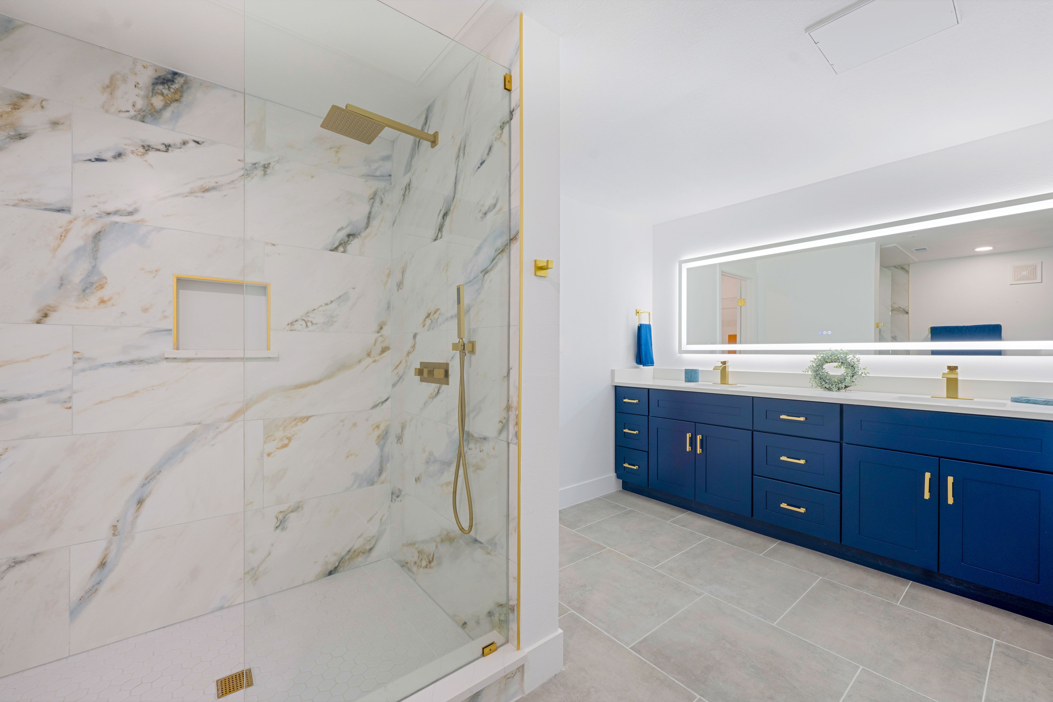 Spa-style bathroom with marble shower, gold fixtures, and navy double vanity
