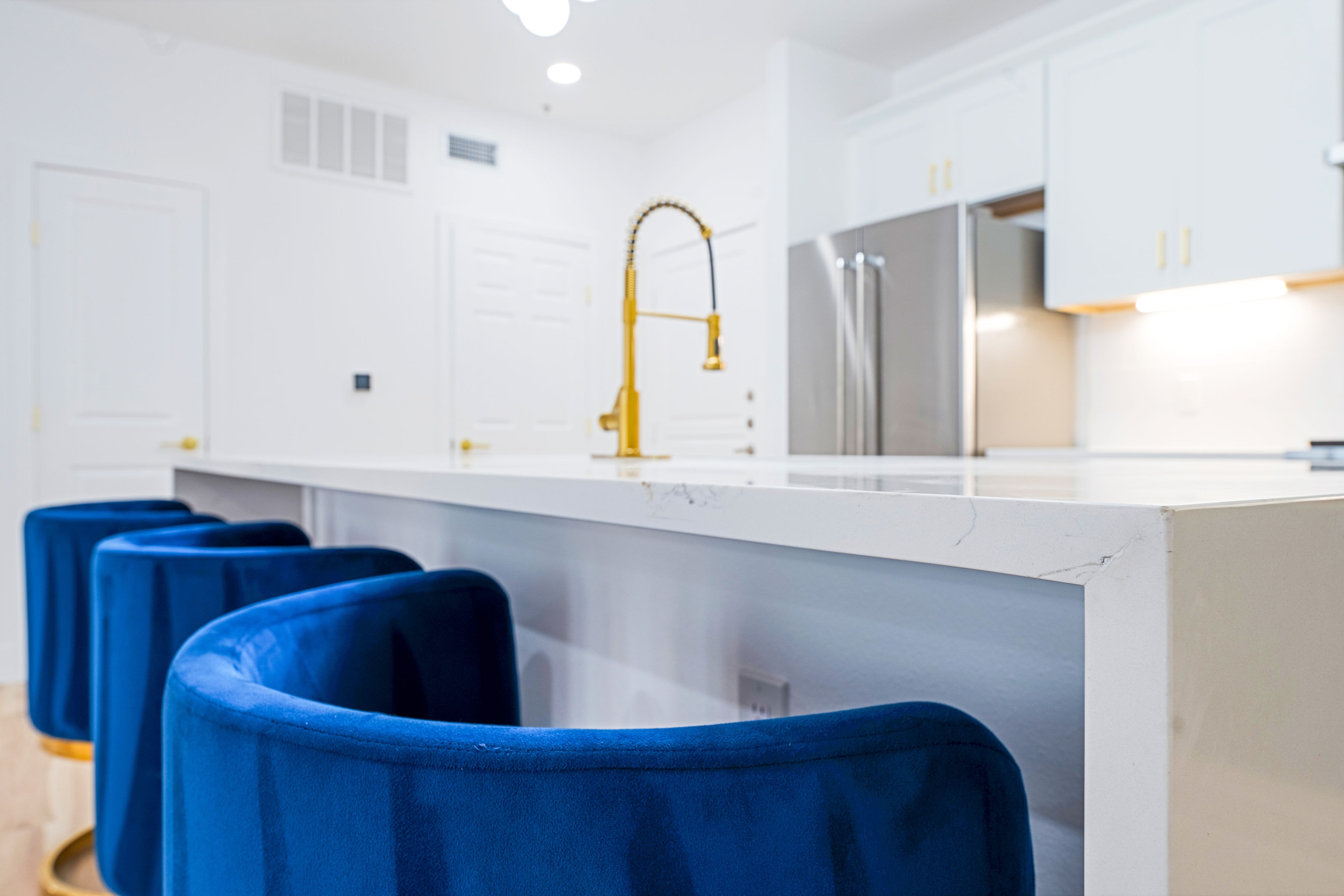 Close-up of kitchen island with blue bar stools and gold faucet