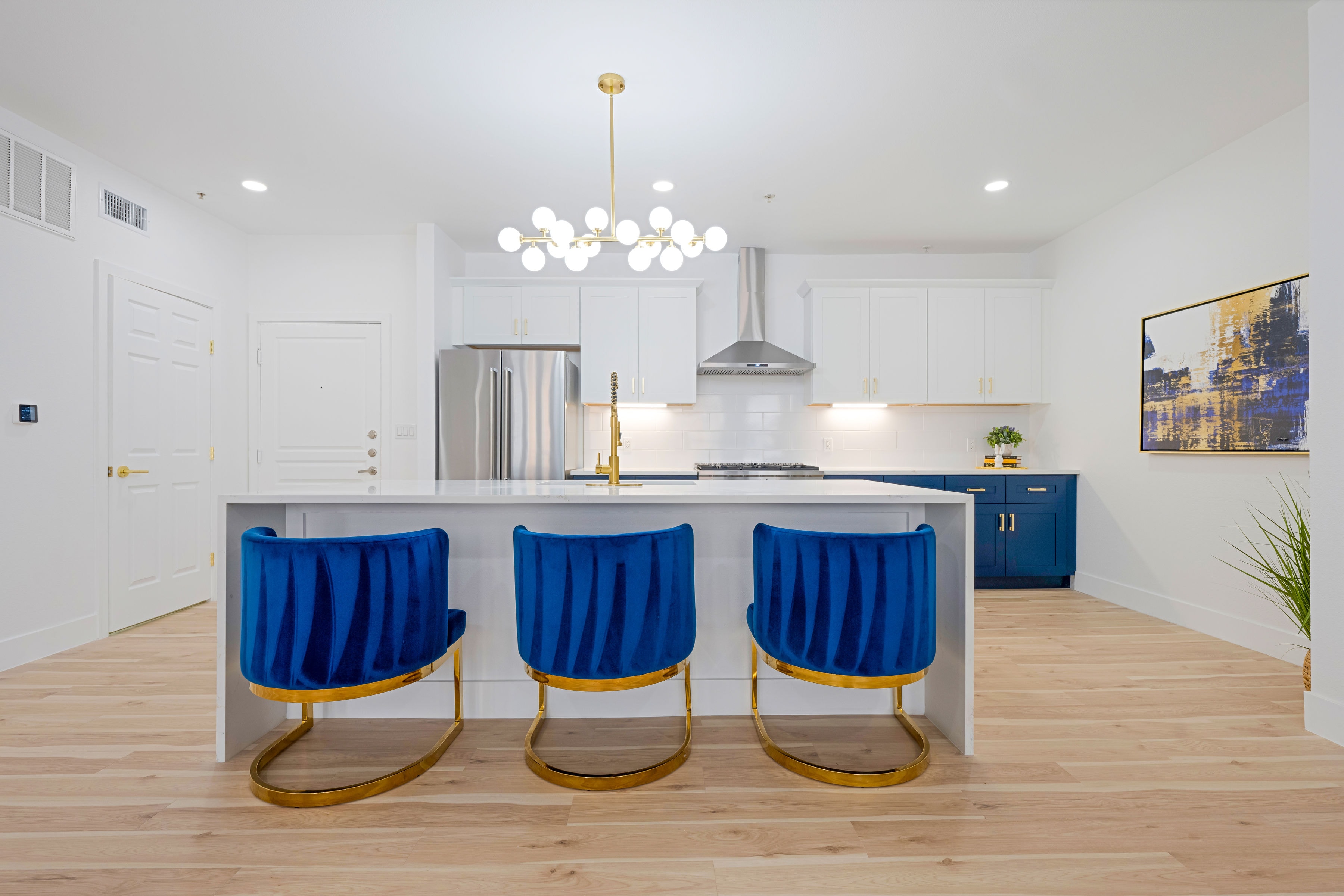 Kitchen island with blue velvet bar stools and gold legs under a globe chandelier