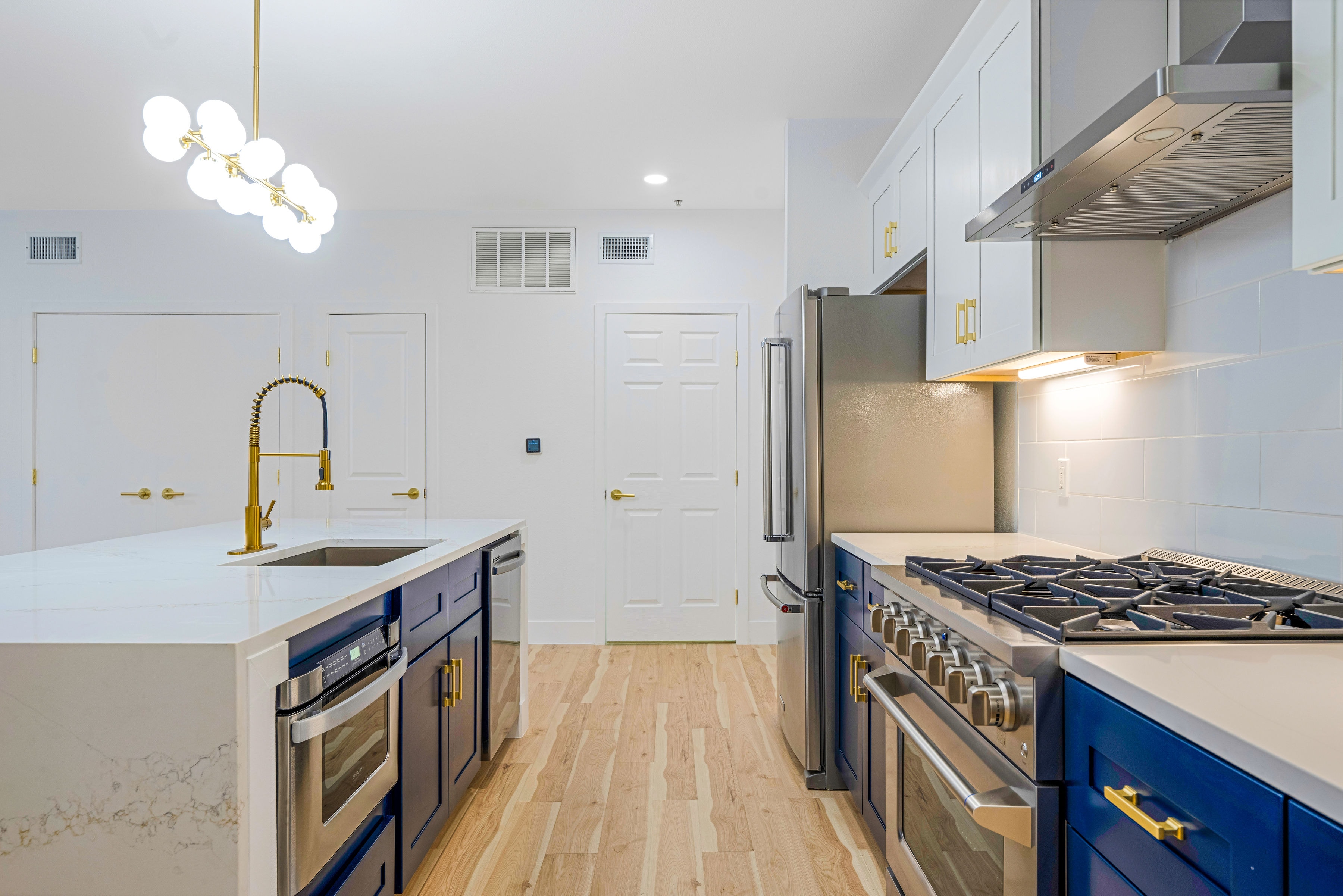 Wide kitchen view with navy lower cabinets, gold faucet, and modern chandelier